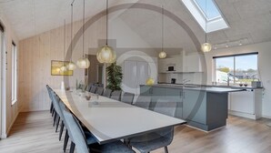 A modern kitchen with a central island, a dining area with a long table and chairs, and a skylight above. - Luxurious home in Krakow am See (Krakow am See)