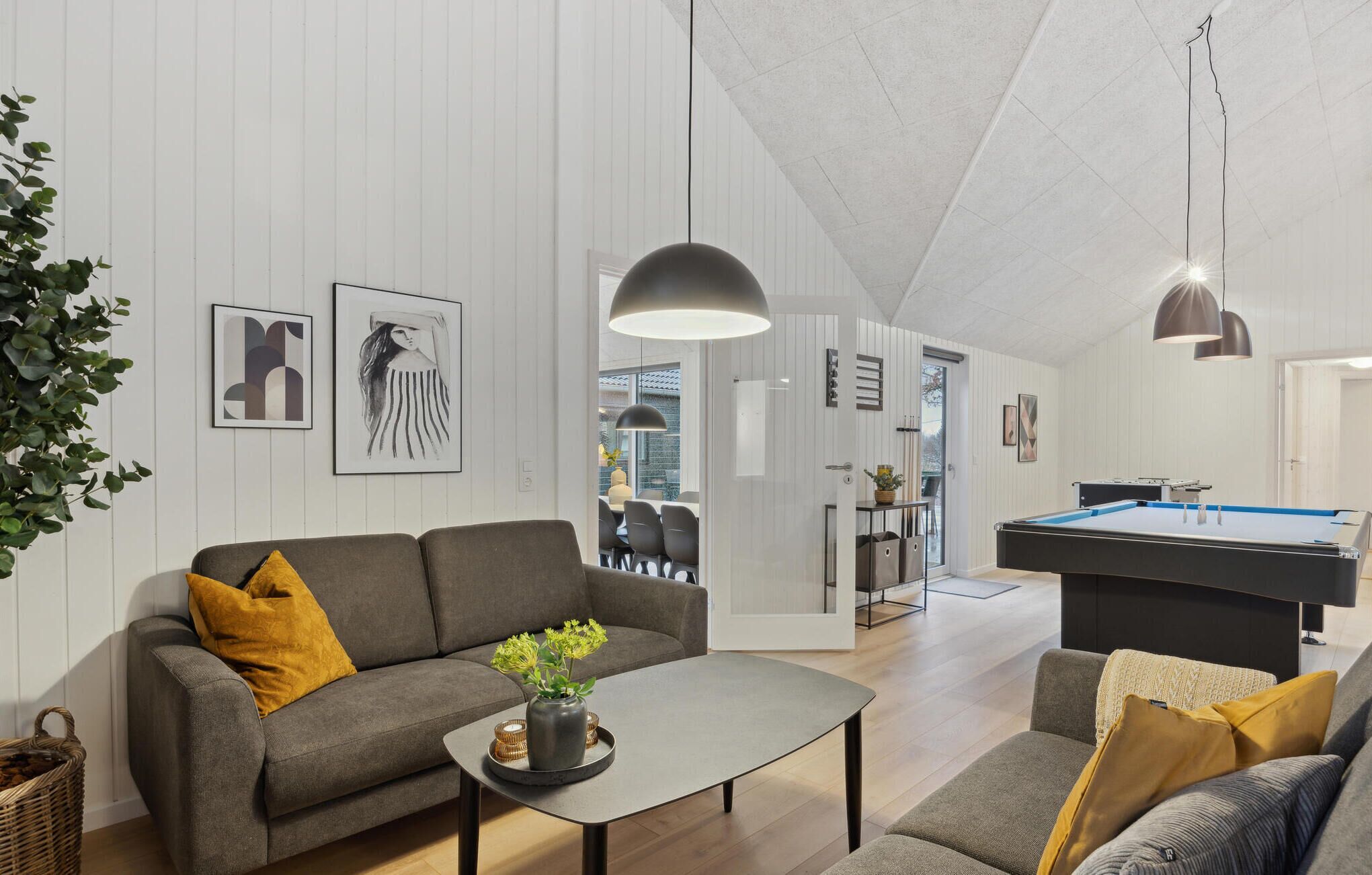 A modern living room with a pool table, grey sofas, and artwork on the walls.