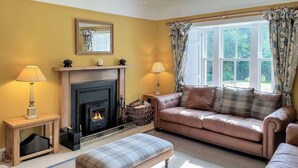 A cozy living room with a fireplace, a sofa, an ottoman, and a window with curtains. - The Old Manse - UKC6854 (Glenclova, near Kirriemuir)