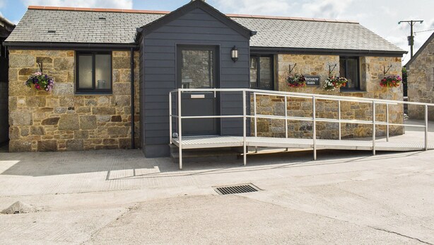 A stone building with a grey door, windows, and a metal ramp leading to the entrance.