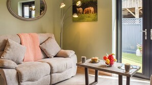 A living room with a sofa, a coffee table with fruits and a cup, a mirror, and a painting of cows.