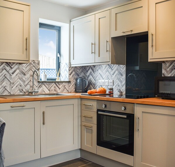 A modern kitchen with light-colored cabinets, a herringbone-patterned backsplash, a window, and a built-in oven. - 1 bedroom accommodation in Trewardreva, near Constantine (Trewardreva, near Constantine)