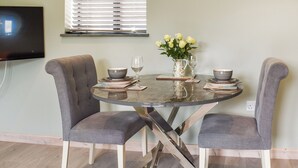 A dining table with two chairs, a vase with flowers, and a flat-screen TV mounted on the wall.