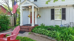 A two-story house with a covered porch, a red chair, and a small garden.
