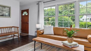 A living room with a wooden bench, a sofa, a coffee table, and a large window with a view of greenery.