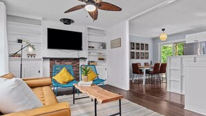 A modern living room with a sofa, a coffee table, and a fireplace. There is a dining area with a table and chairs.