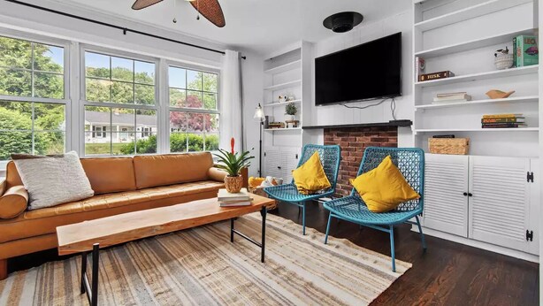 A modern living room with a leather sofa, blue wicker chairs, a fireplace, and a large TV.