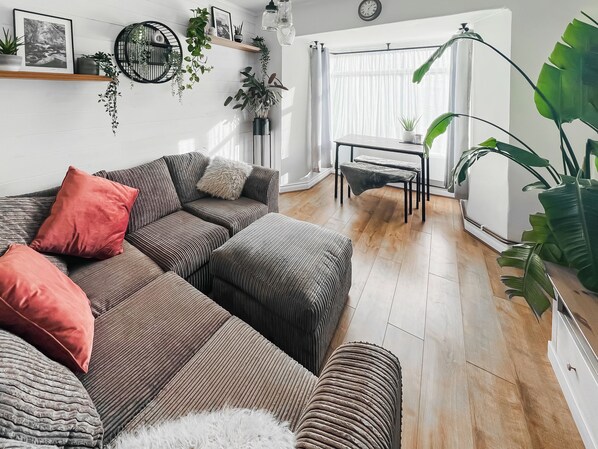 A modern living room with a sectional sofa, a small table, and various plants. - The Annex at Tenniside (Perranporth)
