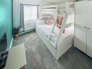 A bunk bed room with a desk, a radiator, a window with curtains, and a potted plant. - The Annex at Tenniside (Perranporth)