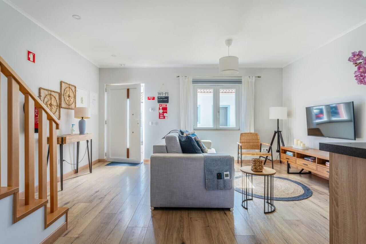 Een moderne woonkamer met een grijze bank, houten vloeren, een televisie en een trap.