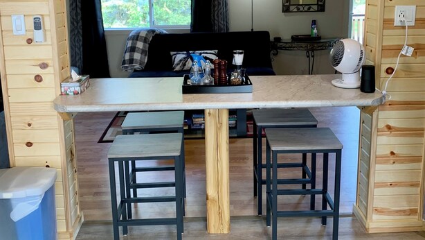 A wooden interior with a central dining table, two chairs, a sofa, and a ceiling light fixture.