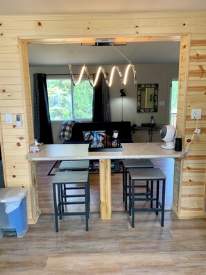 A wooden interior with a central dining table, two chairs, a sofa, and a ceiling light fixture.