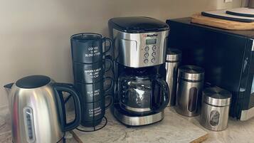 En køkkenbordplade med en kaffemaskine, en elkedel og to rustfrie stålbeholdere.