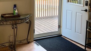 A room with a wooden deck, a door with a glass panel, a small table with a bottle, and a mirror on the wall.