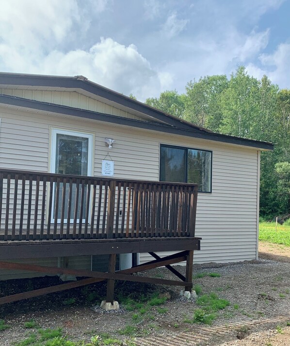 A small, single-story mobile home with a wooden deck in front.
