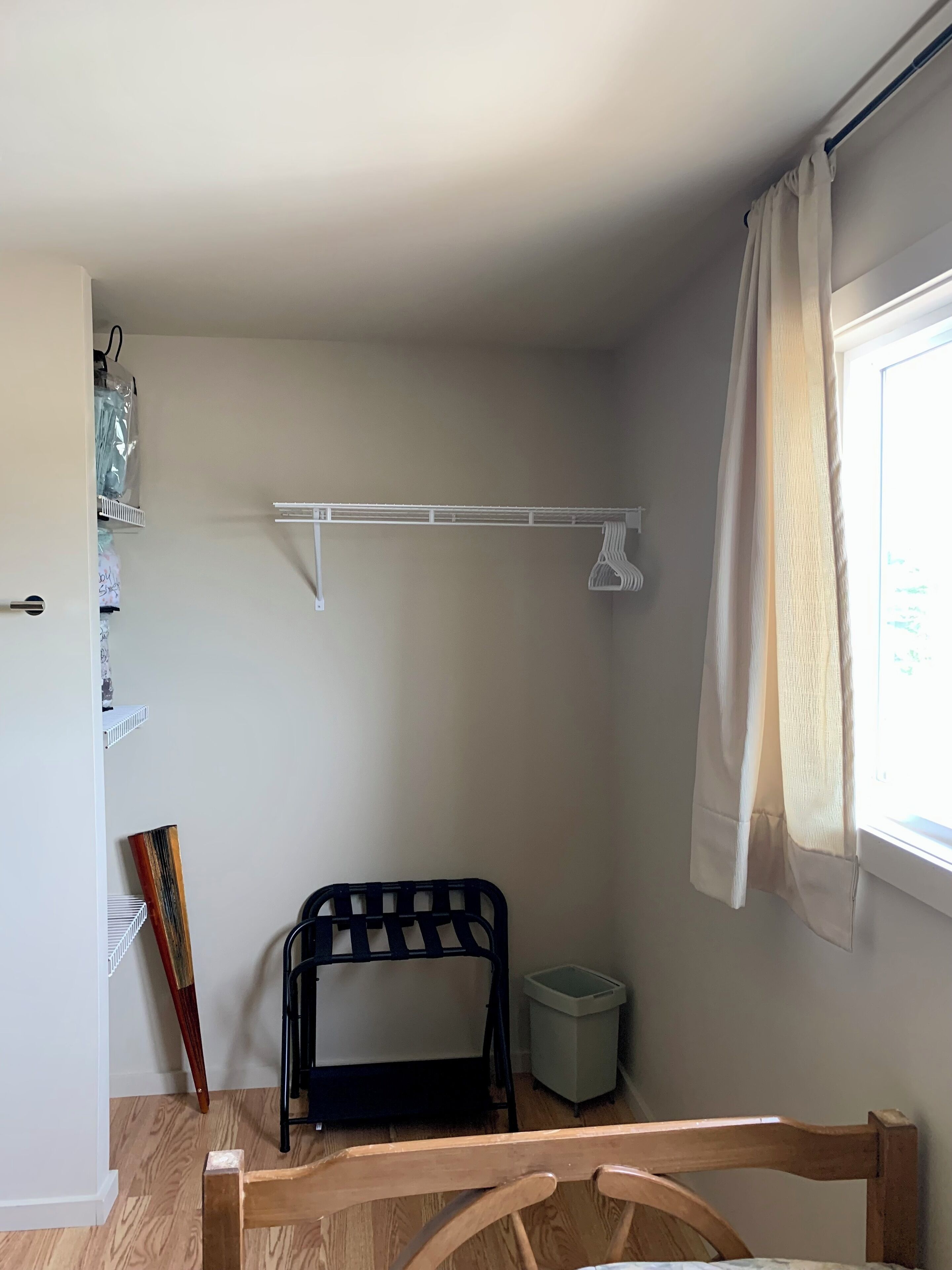 A small, well-lit room with a wooden chair, a black bench, a white shelf, and a window with curtains.