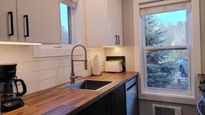 A modern kitchen with a wooden countertop, stainless steel sink, and a window with a view of trees and a car. - Chalet Escapade Orford - Great golf and ski escape 5 minutes from Mont-Orford (Orford)
