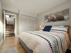 Quarto com cama, guarda-roupa, escada e um quadro de urso na parede.