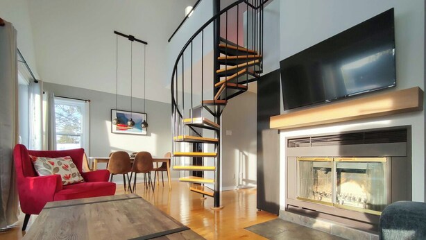 A modern living room with a spiral staircase, a fireplace, and a red sofa. - Chalet Escapade Orford - Great golf and ski escape 5 minutes from Mont-Orford (Orford)