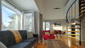 A modern living room with a sofa, red chair, dining table, and a staircase. - Chalet Escapade Orford - Great golf and ski escape 5 minutes from Mont-Orford (Orford)