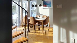 A modern dining area with a wooden table and chairs, a staircase, and large windows allowing natural light. - Chalet Escapade Orford - Great golf and ski escape 5 minutes from Mont-Orford (Orford)