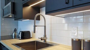 Een moderne keuken met een roestvrijstalen spoelbak, een waterkoker en een broodrooster. Op het aanrecht staan twee zwarte bakken met de tekst 'THE' en 'CAFE'.