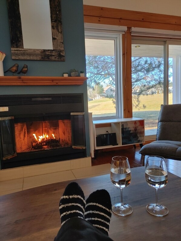 Una sala de estar acogedora con chimenea, vistas al exterior y una mesa con vasos.