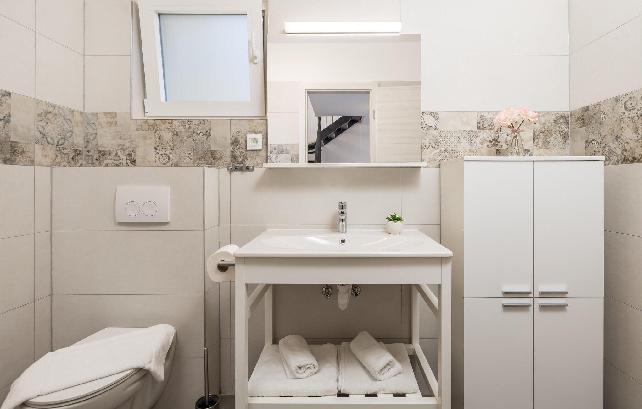 Une salle de bain moderne avec un lavabo blanc, un miroir au-dessus, une petite plante en pot et un porte-serviettes.