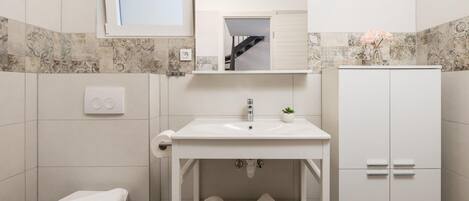 Une salle de bain moderne avec un lavabo blanc, un miroir au-dessus, une petite plante en pot et un porte-serviettes.