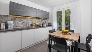 Een moderne keuken met een ingebouwde kookplaat, een koffiezetapparaat en een magnetron. Er staat een eettafel met stoelen en er is een raam met gordijnen.