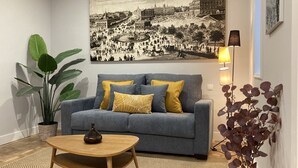 A living room with a grey sofa, yellow cushions, a wooden coffee table, a large black and white cityscape painting, a potted plant, and a floor lamp. - Housing Sol by Sharing Co (Madrid)