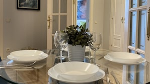 A dining area with a glass table, white plates, and wine glasses. There is a potted plant in the center. - Housing Sol by Sharing Co (Madrid)