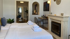 A hotel room with a large bed, a fireplace, a desk with a chair, and a dining area visible through an open door. - Housing Sol by Sharing Co (Madrid)