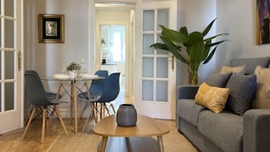 A living room with a grey sofa, blue chairs, a small wooden table, and a large green plant. - Housing Sol by Sharing Co (Madrid)