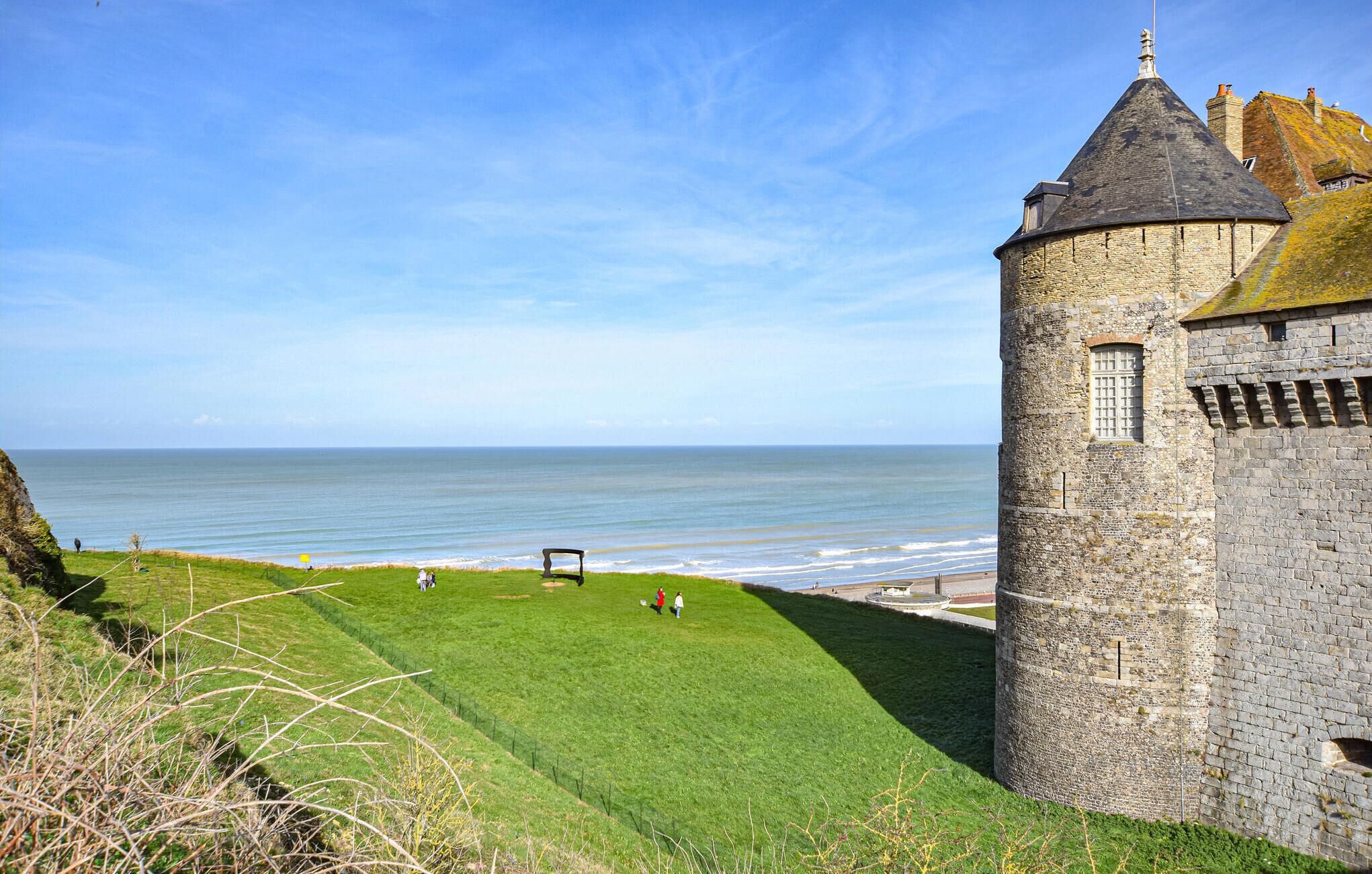 A coastal castle with a grassy foreground and a view of the sea.
