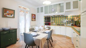 Cucina con mobili bianchi, un tavolo da pranzo per quattro persone e una parete rivestita di piastrelle.