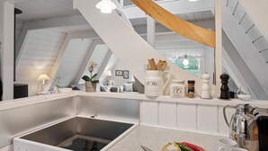 Une cuisine moderne dotée d’une cuisinière intégrée, d’un plan de travail avec ustensiles de cuisine, et offrant une vue sur l’espace de vie grâce à une grande fenêtre.
