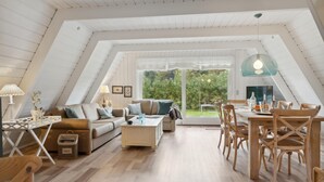 Un loft spacieux avec un plafond haut, un coin repas, un ensemble de canapés et une vue sur la verdure environnante.