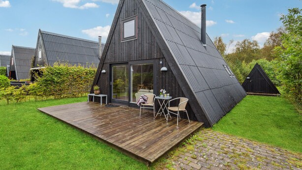 Une maison moderne, de forme triangulaire, dotée d’une terrasse en bois et d’un espace salon extérieur.