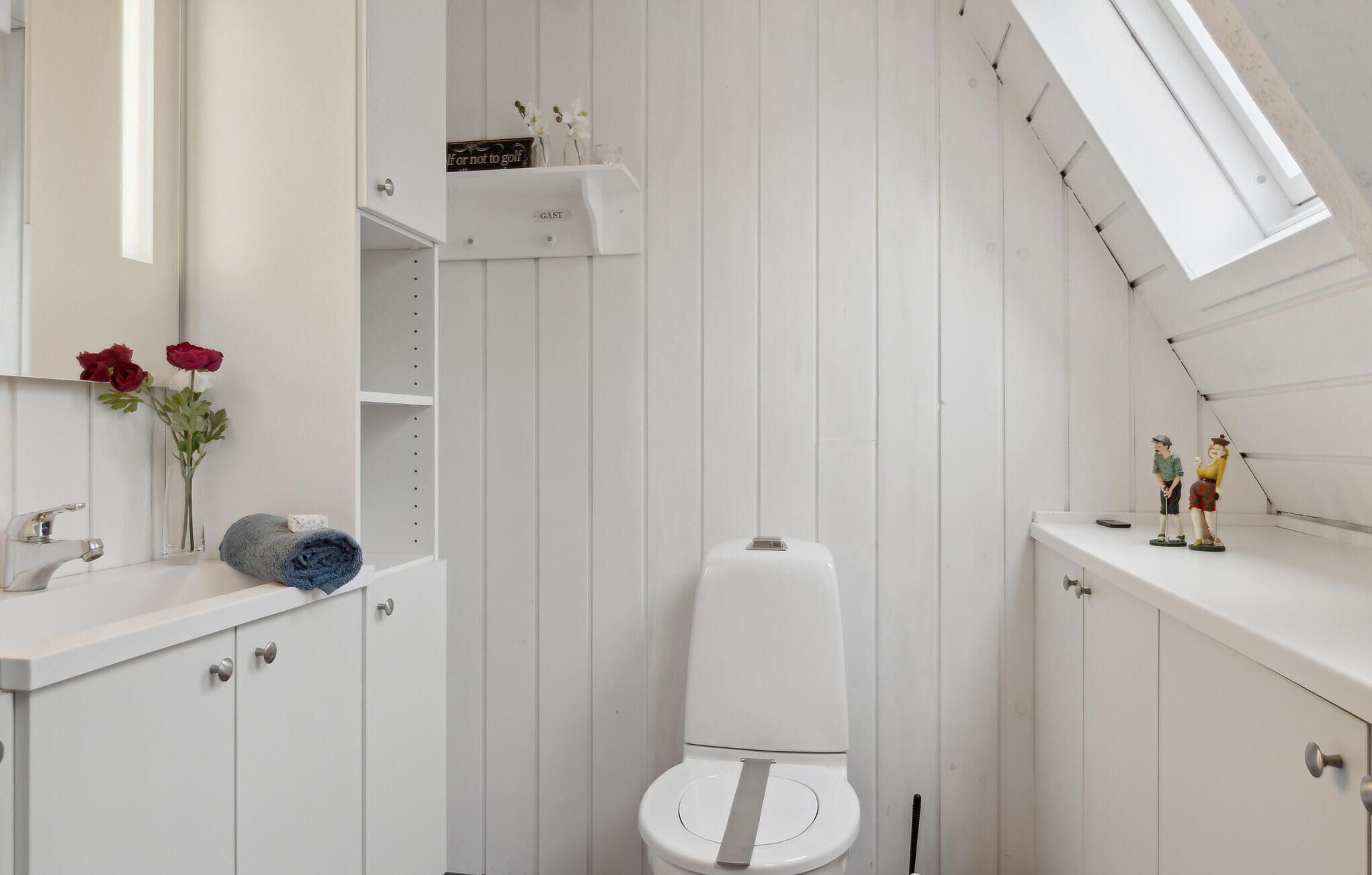 Un baño pequeño con pared a rayas blancas, un inodoro, un lavabo con espejo y un estante con objetos decorativos.