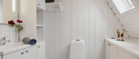 Un baño pequeño con pared a rayas blancas, un inodoro, un lavabo con espejo y un estante con objetos decorativos.
