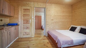 A wooden cabin room with a bed, a small kitchenette, and a door leading to another room. - 1 bedroom awesome apartment in Pogorzelica (Pogorzelica)