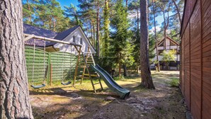 A playground with a slide and swings, surrounded by trees and a house. - 1 bedroom awesome apartment in Pogorzelica (Pogorzelica)
