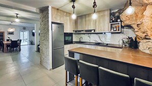 Une cuisine moderne dotée d’un îlot central, de tabourets de bar, d’un mur d’accent en pierre et de luminaires suspendus.