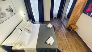 Une chambre d’hôtel avec un lit, un petit tabouret en bois et un tableau accroché au mur.