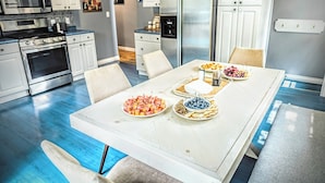 Une cuisine moderne avec des meubles blancs, des appareils en acier inoxydable et une table à manger dressée avec des assiettes de fruits.