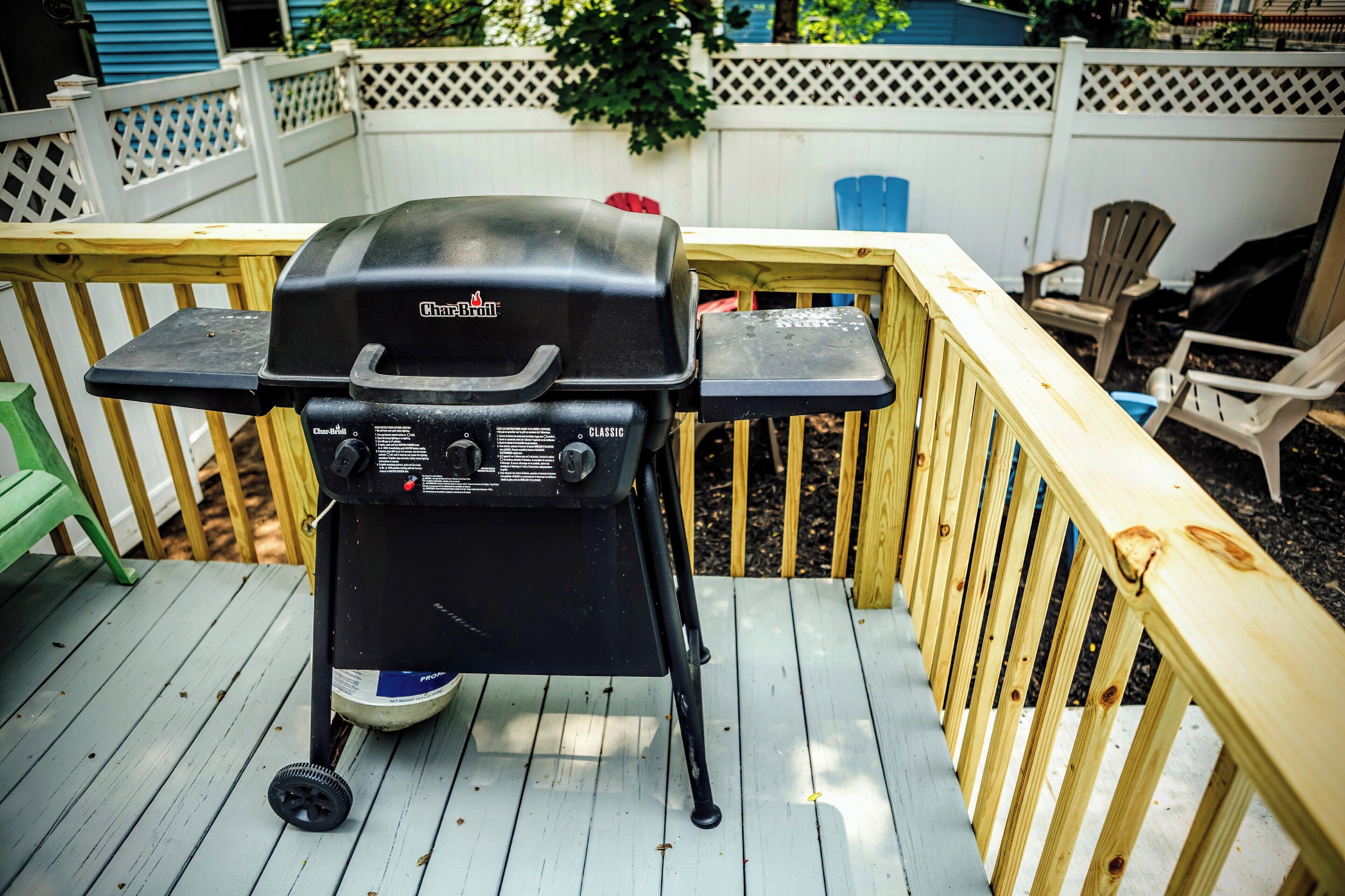 Una parrilla Char-Broil sobre una terraza de madera con una cerca blanca y sillas al fondo.