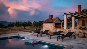 A pool area with lounge chairs, a stone building with a fire pit, and a view of the landscape. - Beautiful home in Pucisca - Praznica (Pucisca - Praznica)