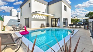 Una casa moderna de dos pisos amb piscina, zona d'estar a l'aire lliure i un porxo cobert.