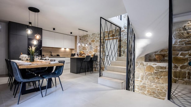 A modern kitchen with a stone wall and a staircase with a geometric railing.